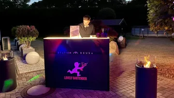 Bartender working at outdoor illuminated bar at night.