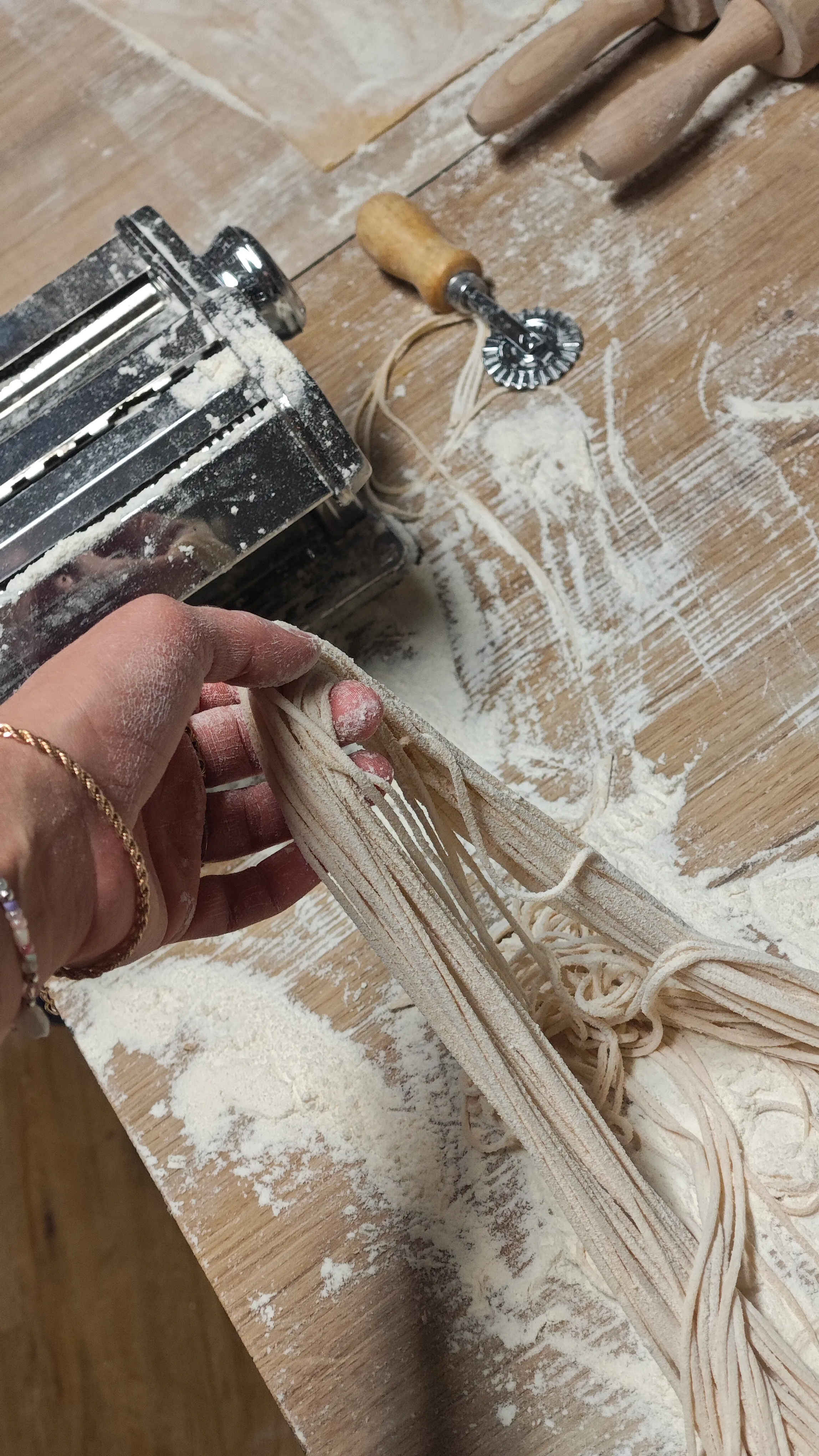 Hand hält frische Pasta neben Nudelmaschine.