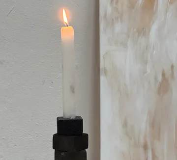 Brennende Kerze auf kunstvollem Halter, abstrakter Hintergrund.