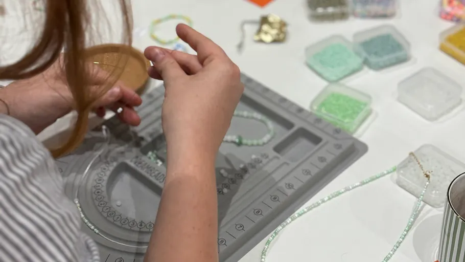 Person making jewelry with beads on table.