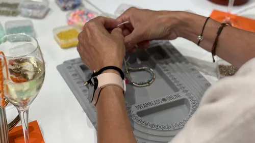 Hände fertigen Schmuck mit Perlen am Tisch.