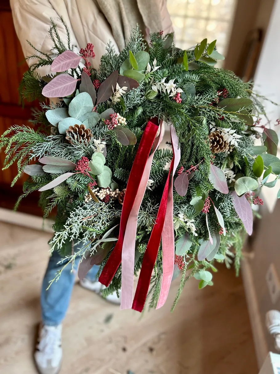 Festive wreath with red ribbons held indoors.
