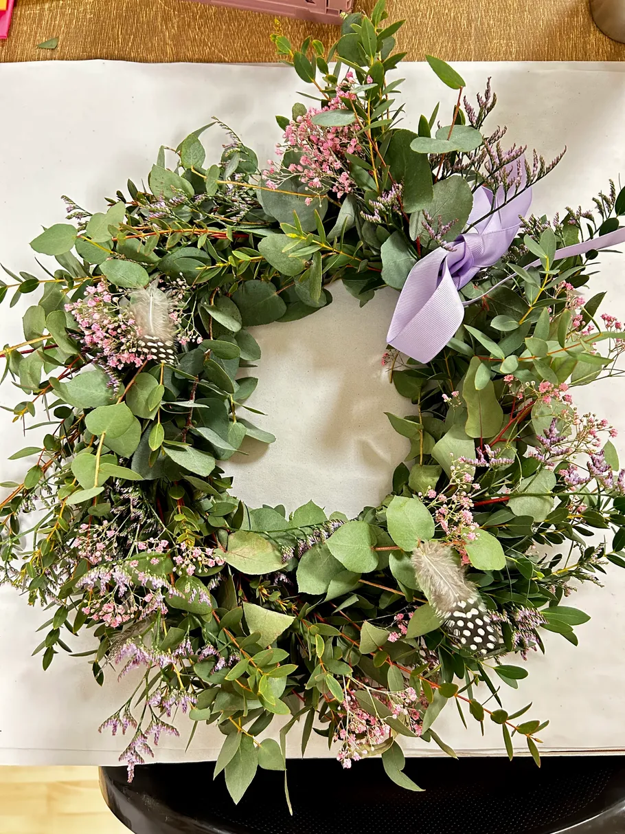 Blumenkranz mit lila Schleife und Federn.