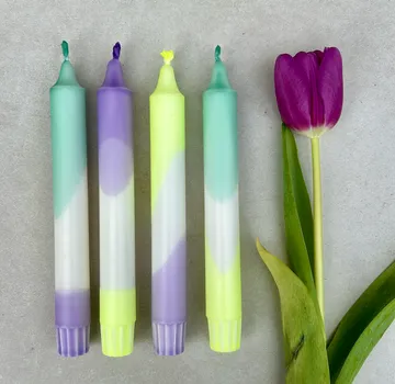 Vier bunte Kerzen neben einer lila Tulpe.