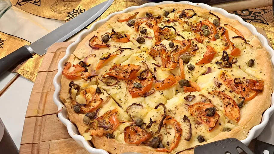 Gemüsepizza auf Holzbrett, Messer daneben.