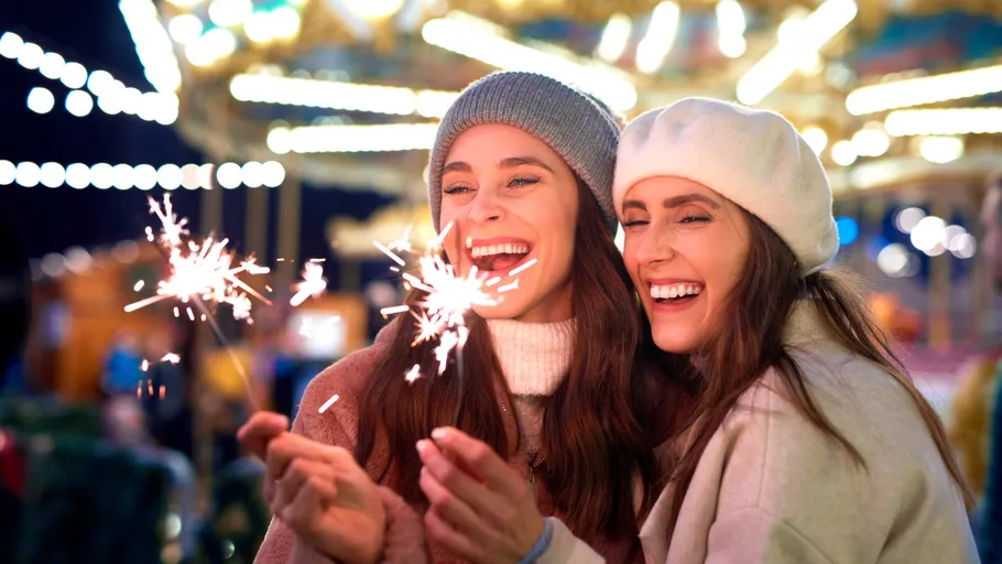 Two women holding sparklers, smiling at night.