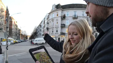 Two people using a tablet on city street.