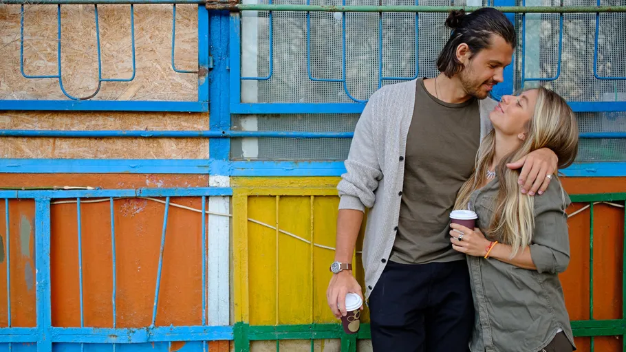 Couple smiling holding coffee cups outdoors.