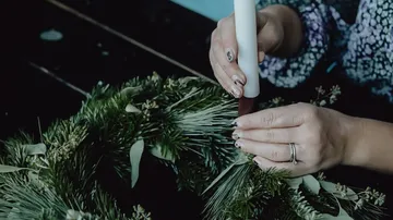 Hands arranging candle in a green wreath.