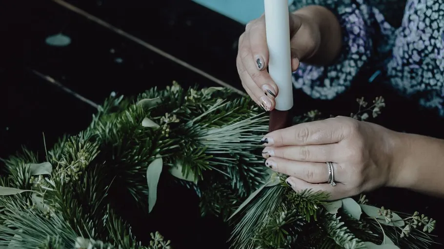 Hände platzieren Kerze in einem grünen Kranz.