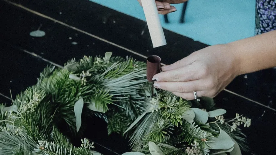 Hands placing candle on green wreath.