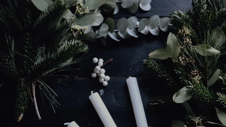 Candles and greenery on a dark table.