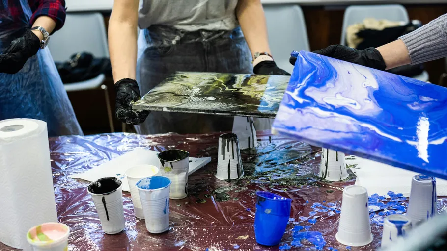 People holding painted canvases, surrounded by paints.