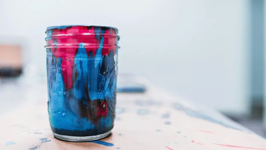 Jar of paint with drips on table.