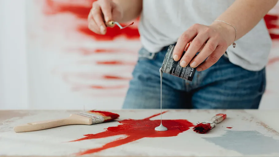 Person gießt Farbe auf rot bemalte Leinwand.