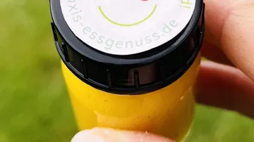 Hand holding yellow bottle outdoors.