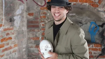 Man holding a skull, smiling, in brick room.