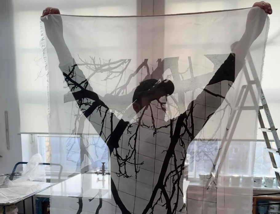Person holding translucent fabric with tree pattern.