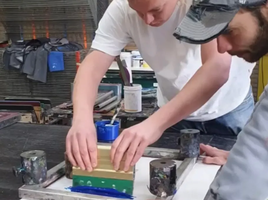 Two people screen printing in workshop.