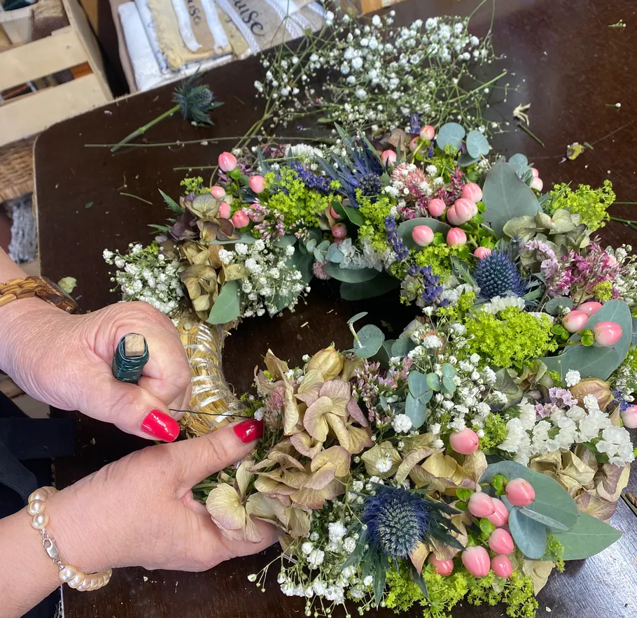Hands crafting floral wreath on table.