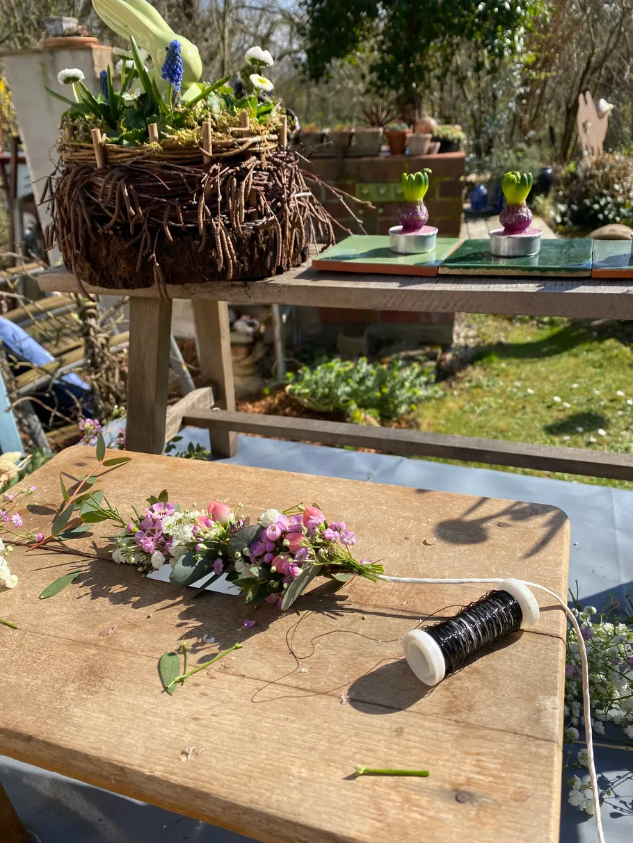 Blumenarrangement auf Tisch mit Garten im Hintergrund.