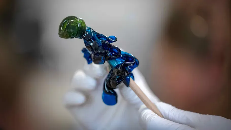 Behandschuhte Hand hält buntes Glasobjekt.