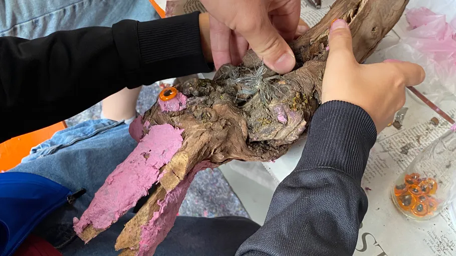Hands working on driftwood sculpture with pink paint.