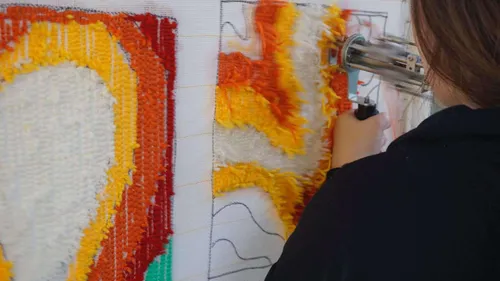 Person using tufting gun on colorful textile.