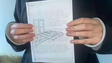 Hände halten Papier mit Schreibmaschinentext und Zeichnung.