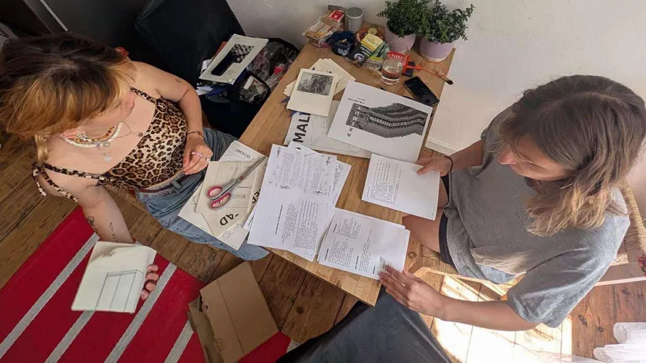 Two people examine papers on a wooden table.
