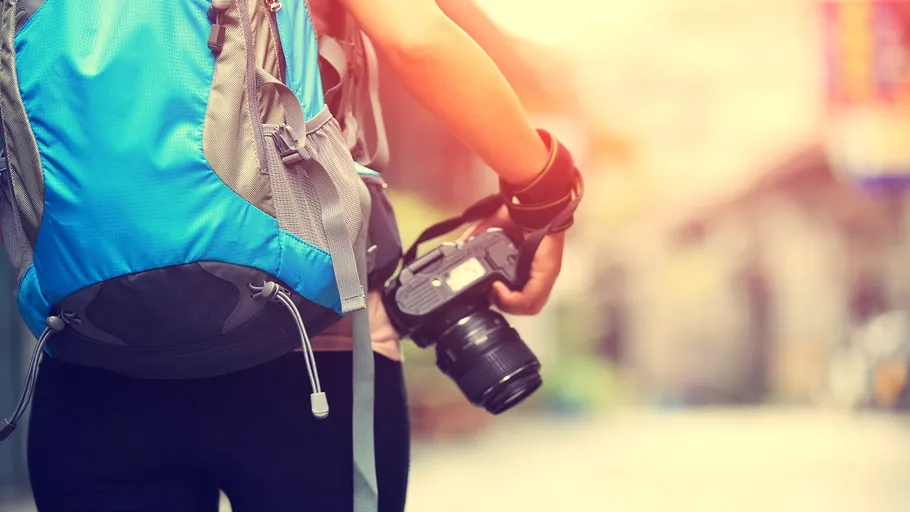 Person with backpack holding camera, outdoor setting.