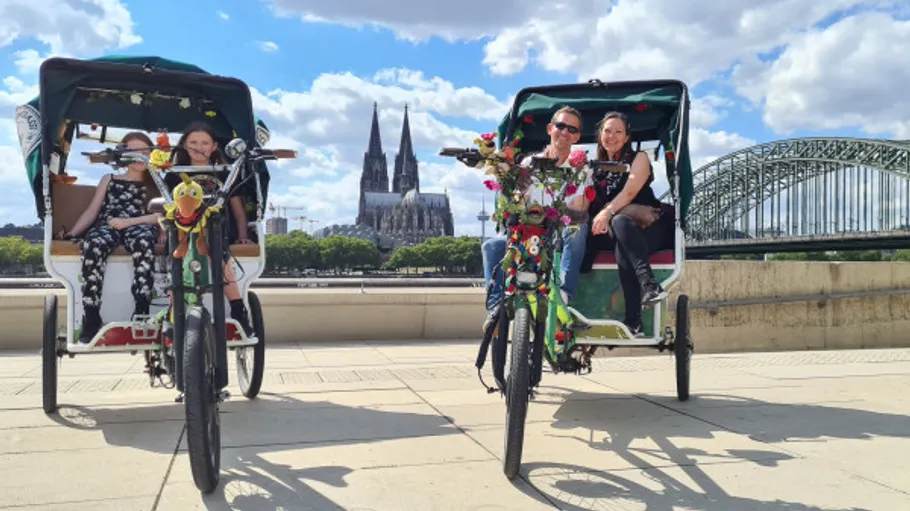 Two rickshaws with passengers near a cathedral.
