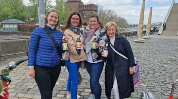 Four women smiling with drinks outdoors.