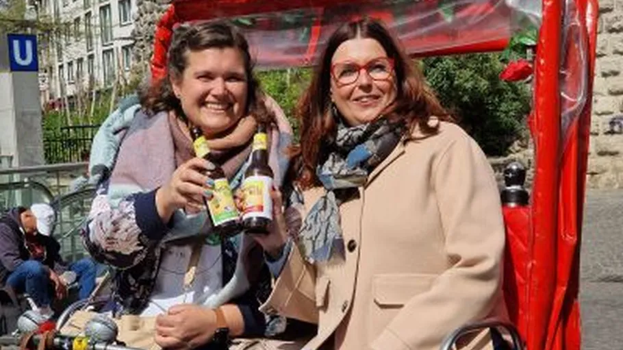 Two women smiling, holding drinks outdoors.