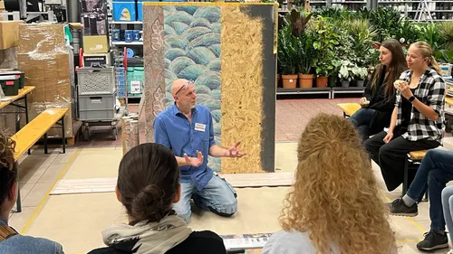 Man kneeling, gesturing, teaches group indoors.