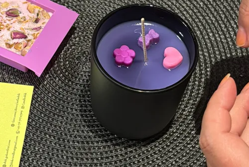 Black candle with colorful wax shapes, on table.