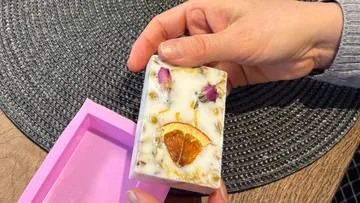 Hand holding handcrafted soap with floral decoration.