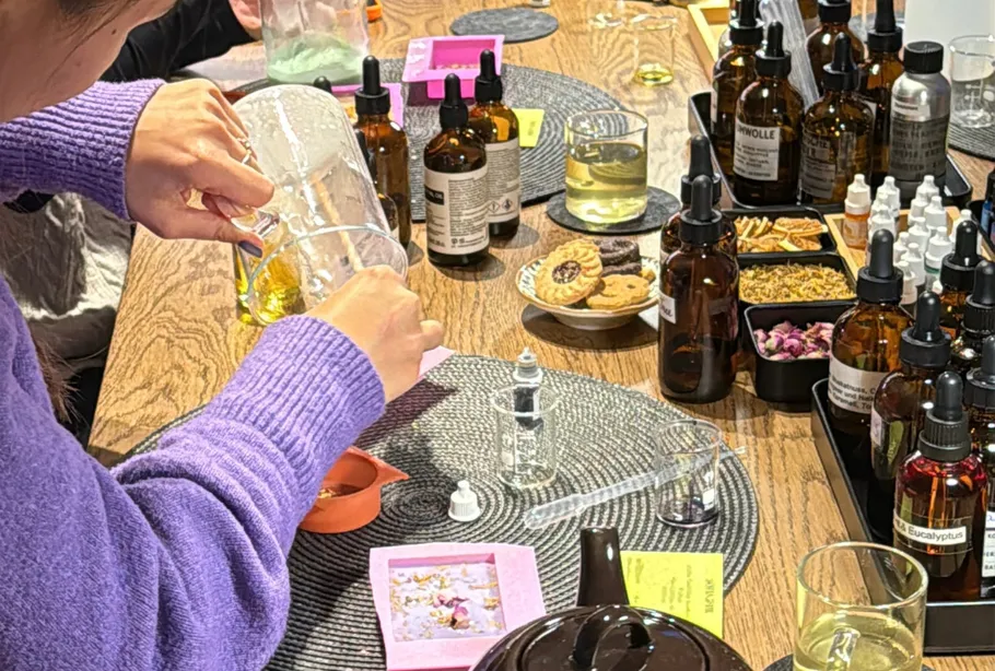 Person mischt Öle und Kräuter auf Tisch.