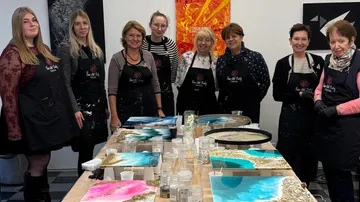 Group of women posing with art projects in studio.
