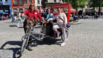 Person with rickshaw and passengers in town square.