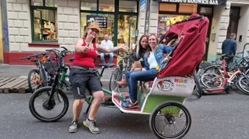 Person riding rickshaw with two seated passengers.