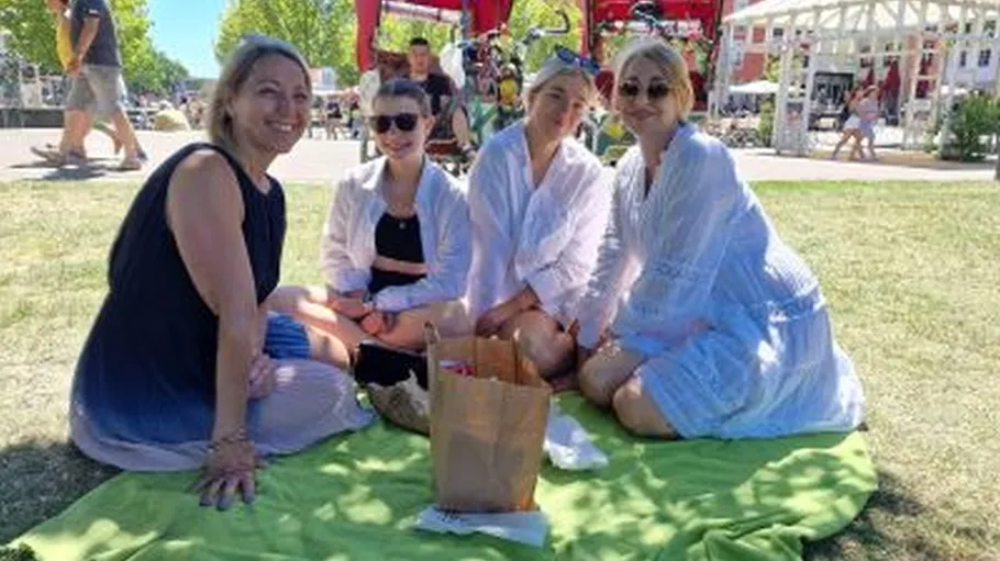 Vier Frauen sitzen auf grünem Decke draußen.