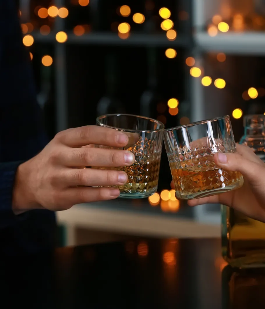 Two hands clinking whiskey glasses indoors.