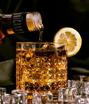 Whiskey wird in Glas mit Zitronenscheibe gegossen.