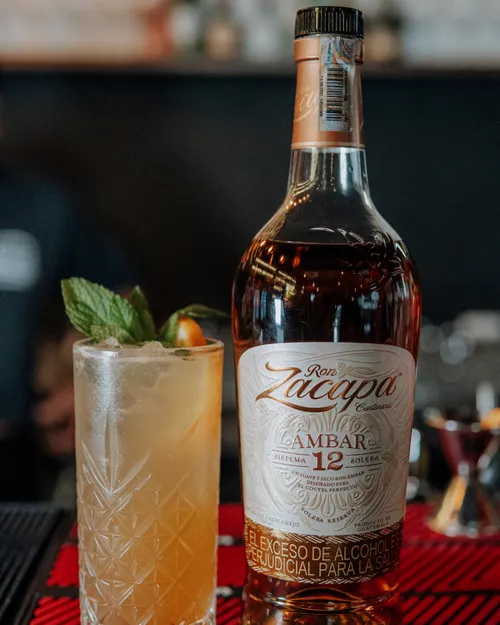 Rum bottle with cocktail on bar countertop.