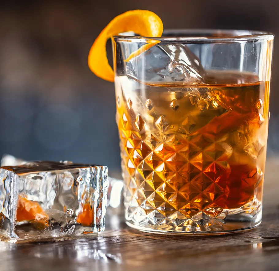 Cocktailglas mit Orangenschale auf Holztisch.