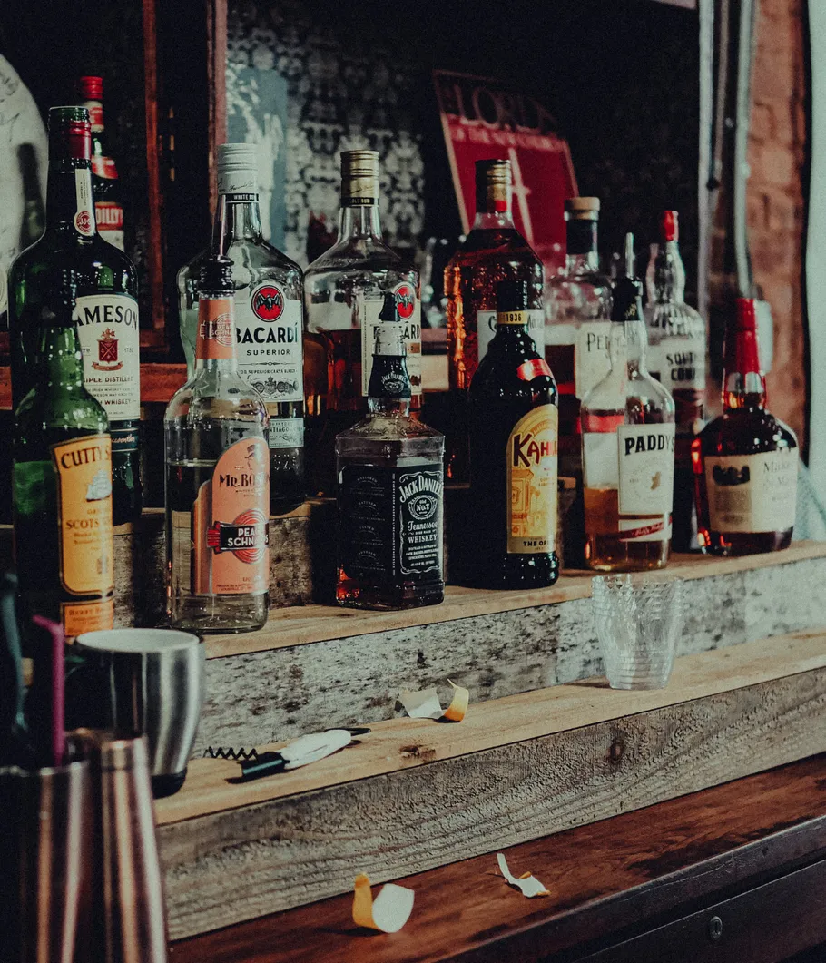 Bottles of liquor on wooden shelf in bar.
