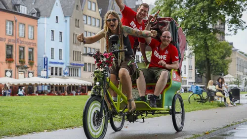 Three people riding a green rickshaw in a city.
