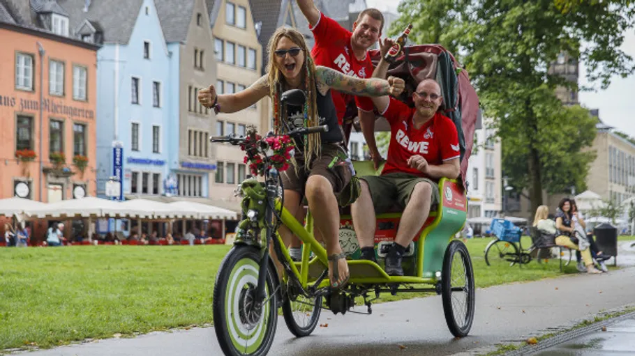 Three people riding a green rickshaw in a city.