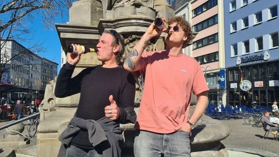 Zwei Personen trinken Bier draußen an sonnigem Tag.